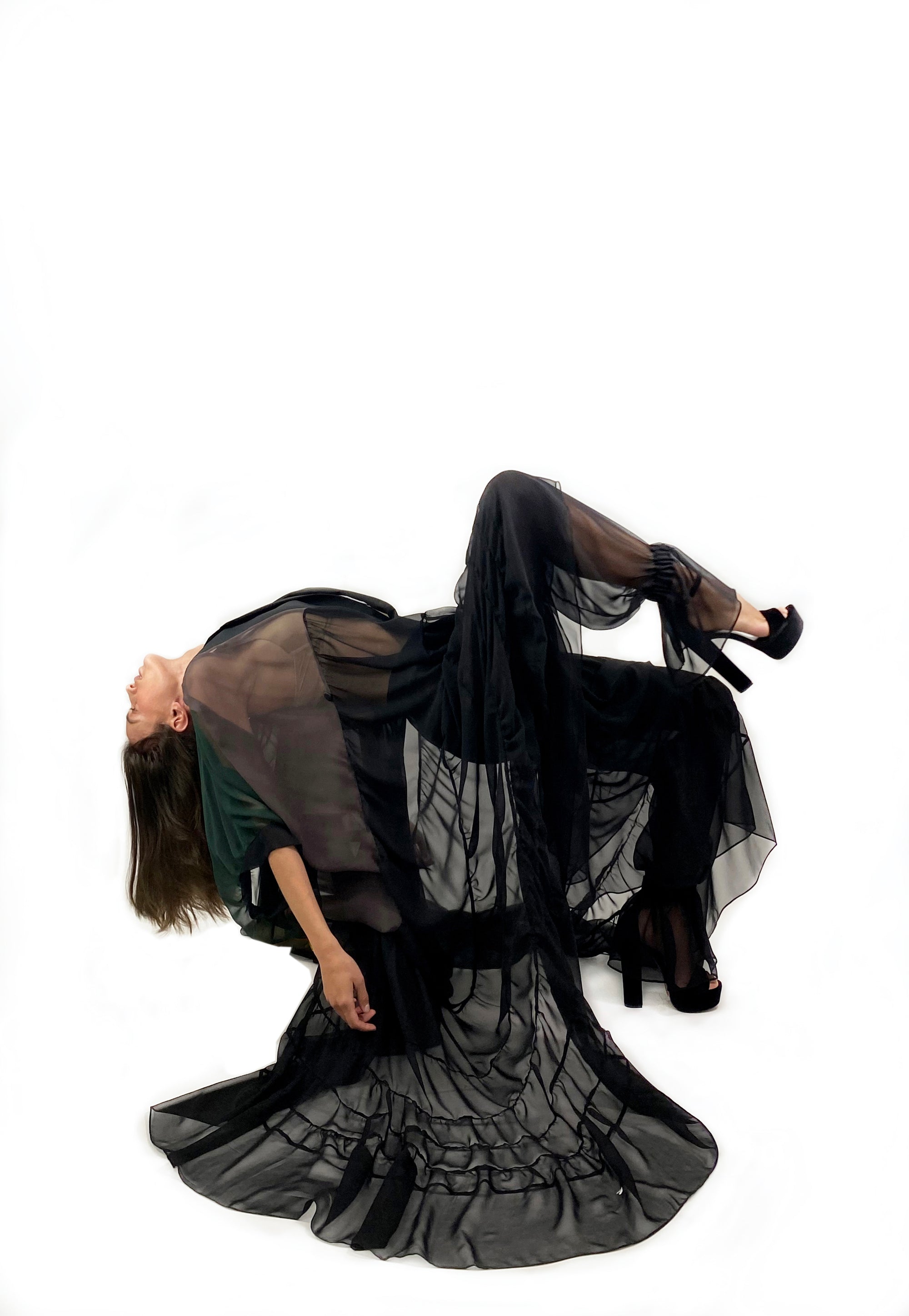 A woman in a black sheer dress reclines on her back, exuding elegance and tranquility in a serene setting.
