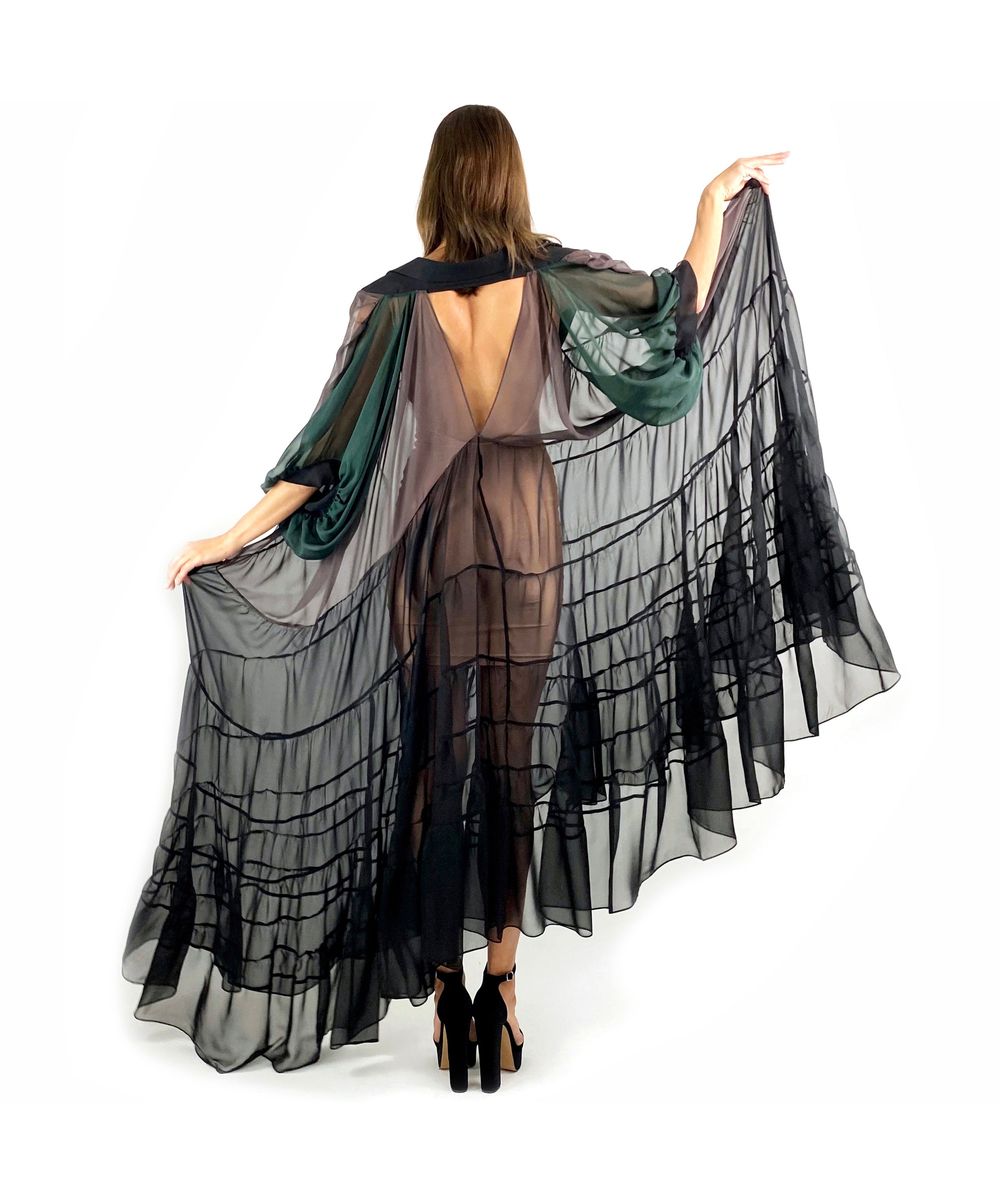 A woman in a sheer black and green dress is seen from the back, showcasing the delicate fabric and her graceful silhouette.