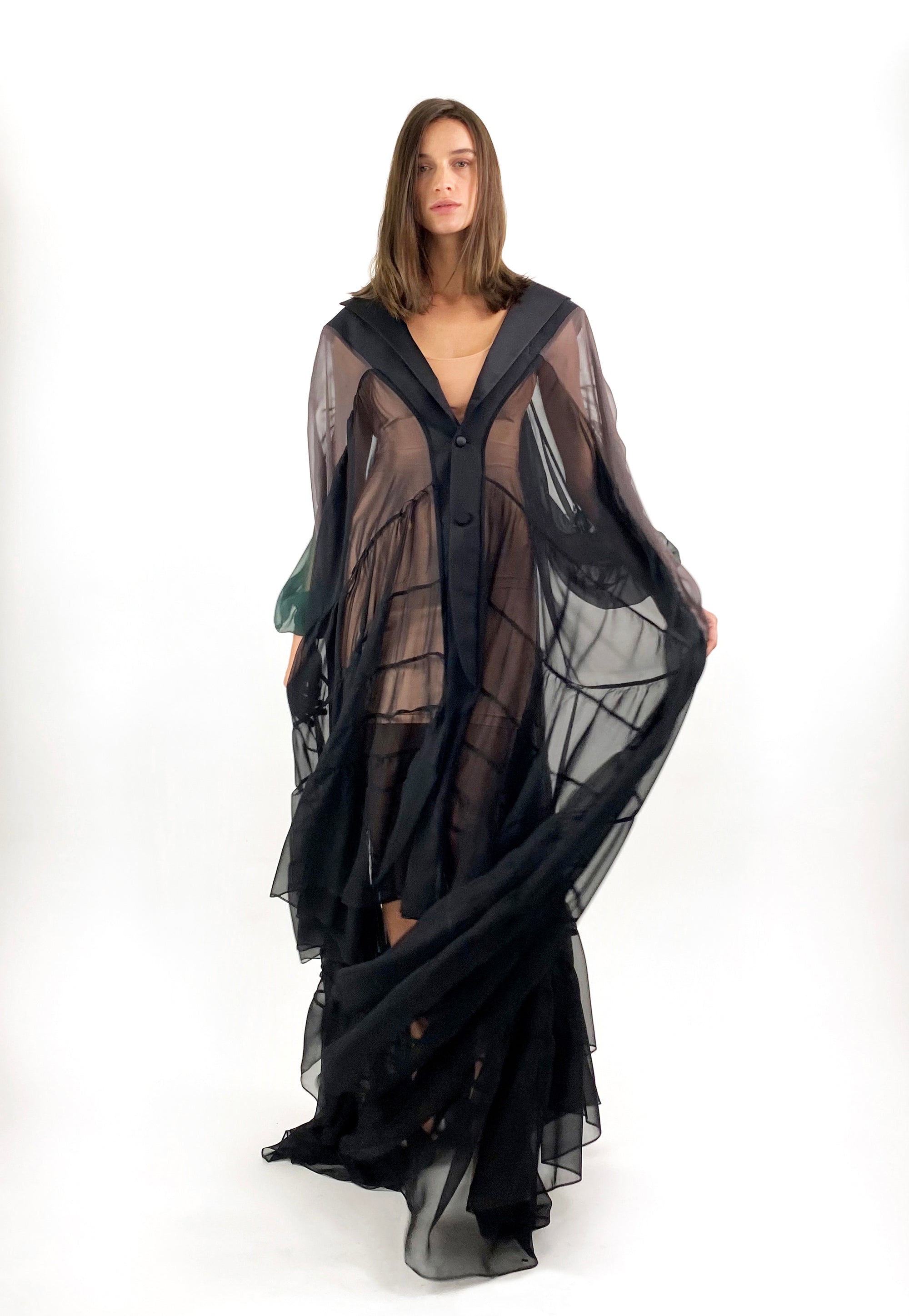 A model showcases a black sheer cape paired with elegant black heels, exuding sophistication and style.