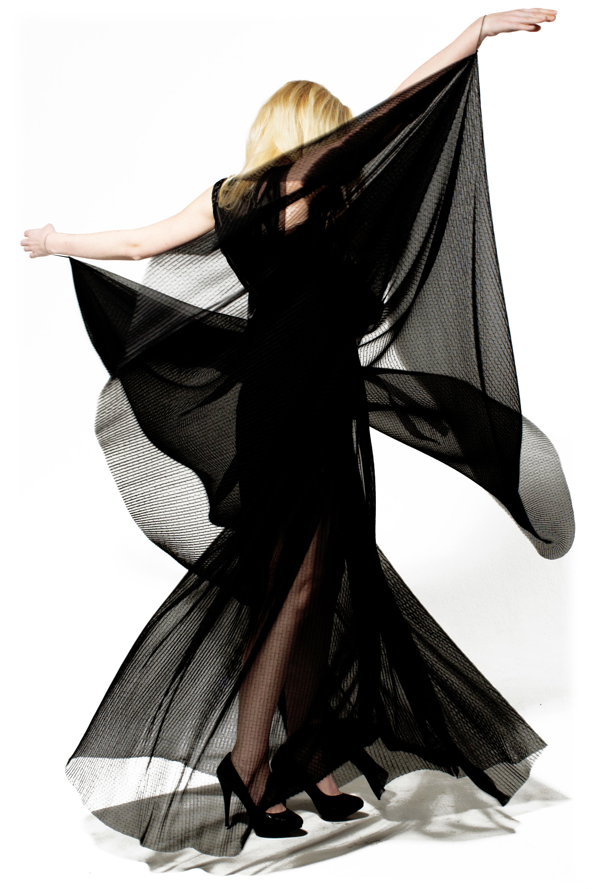 A woman in a sheer black evening dress gracefully dances, showcasing elegance and movement in a captivating performance.