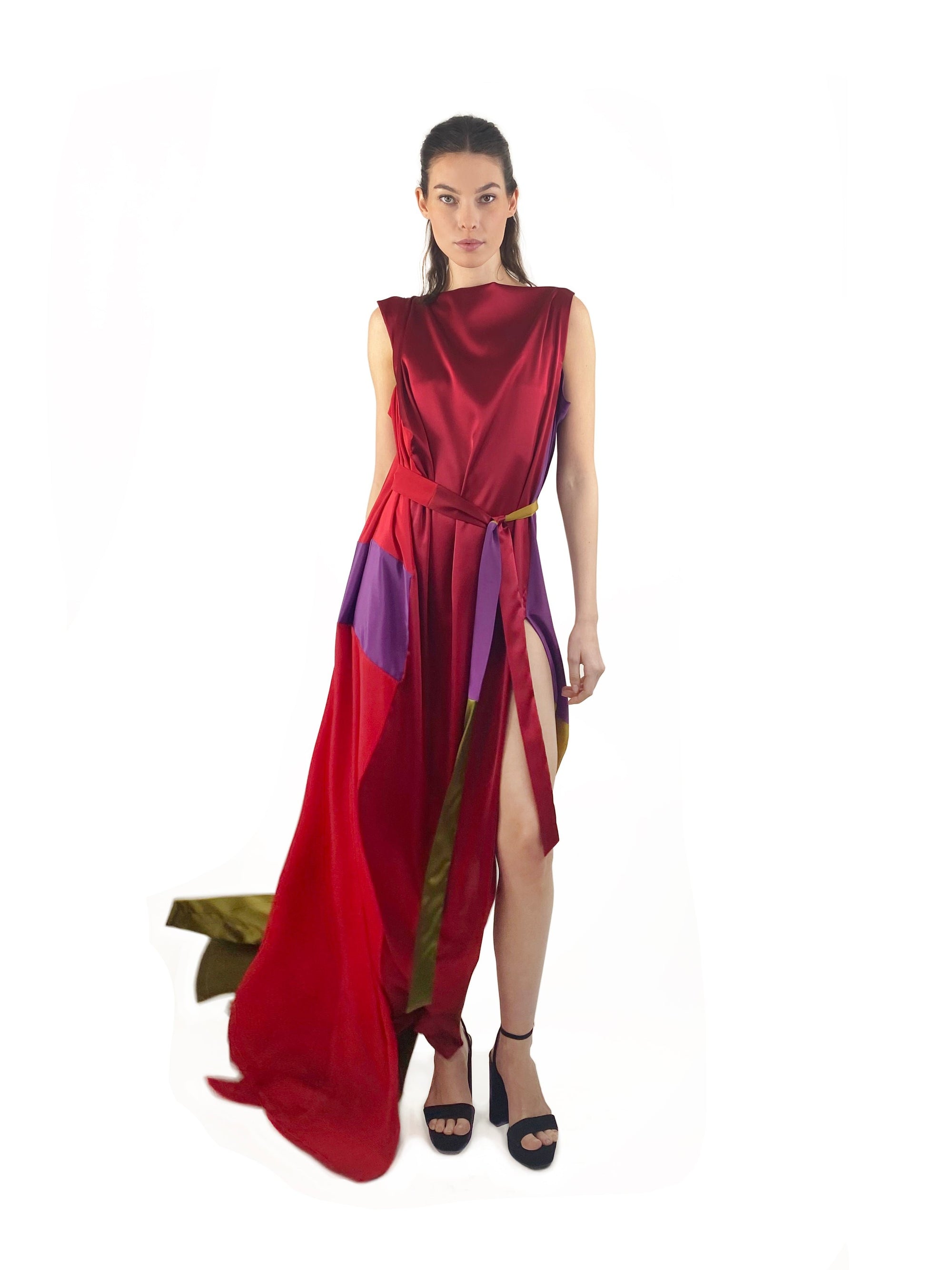A woman wearing a red silk dress adorned with vibrant, multi-colored stripes, standing gracefully against a neutral background.