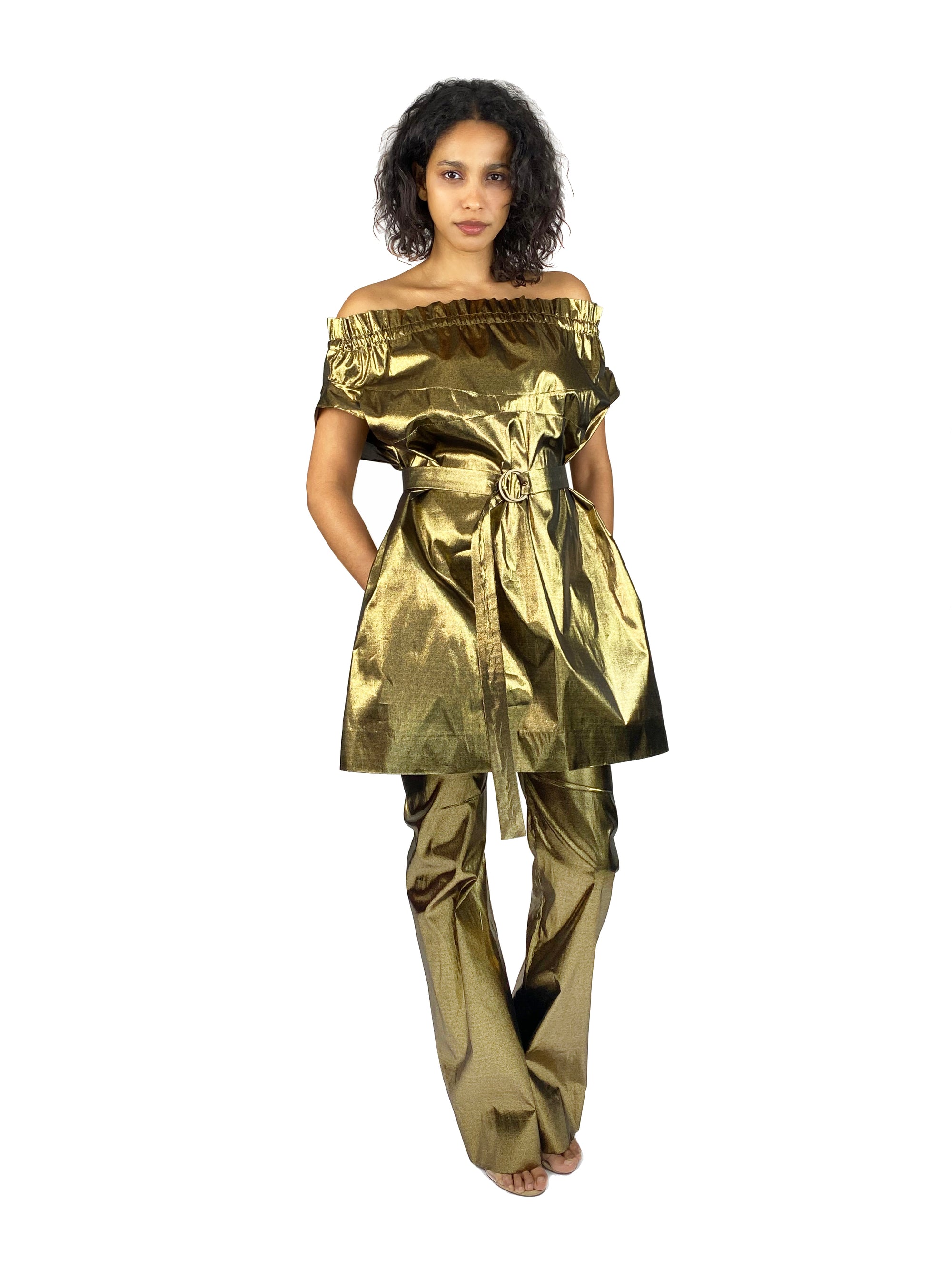 A woman in a golden, strapless overall with a waist-belt stands confidently, exuding modern style and sophistication.