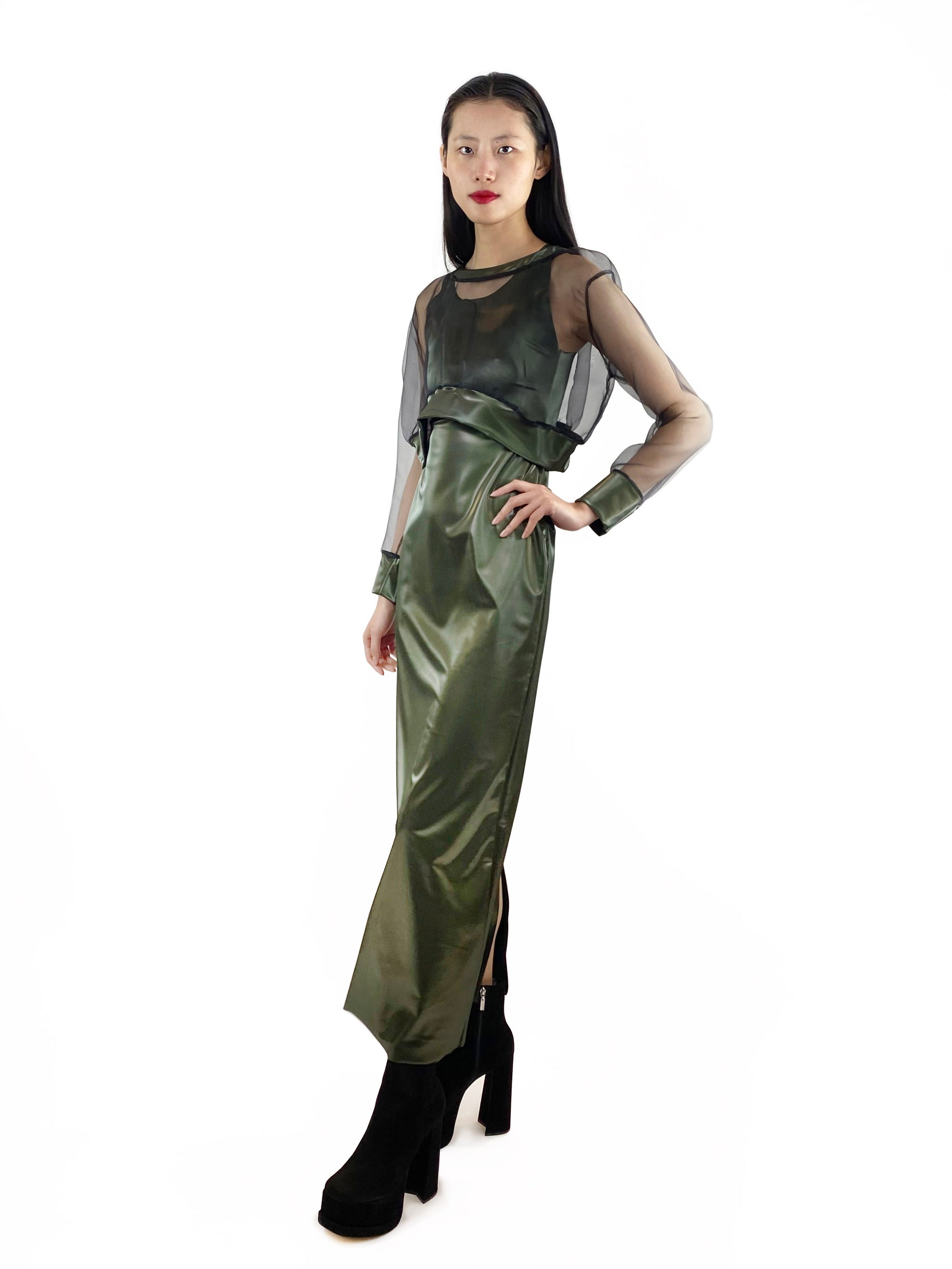 A model wearing a fitted long, green  latex dress featuring a sheer top with latex cuffs. 