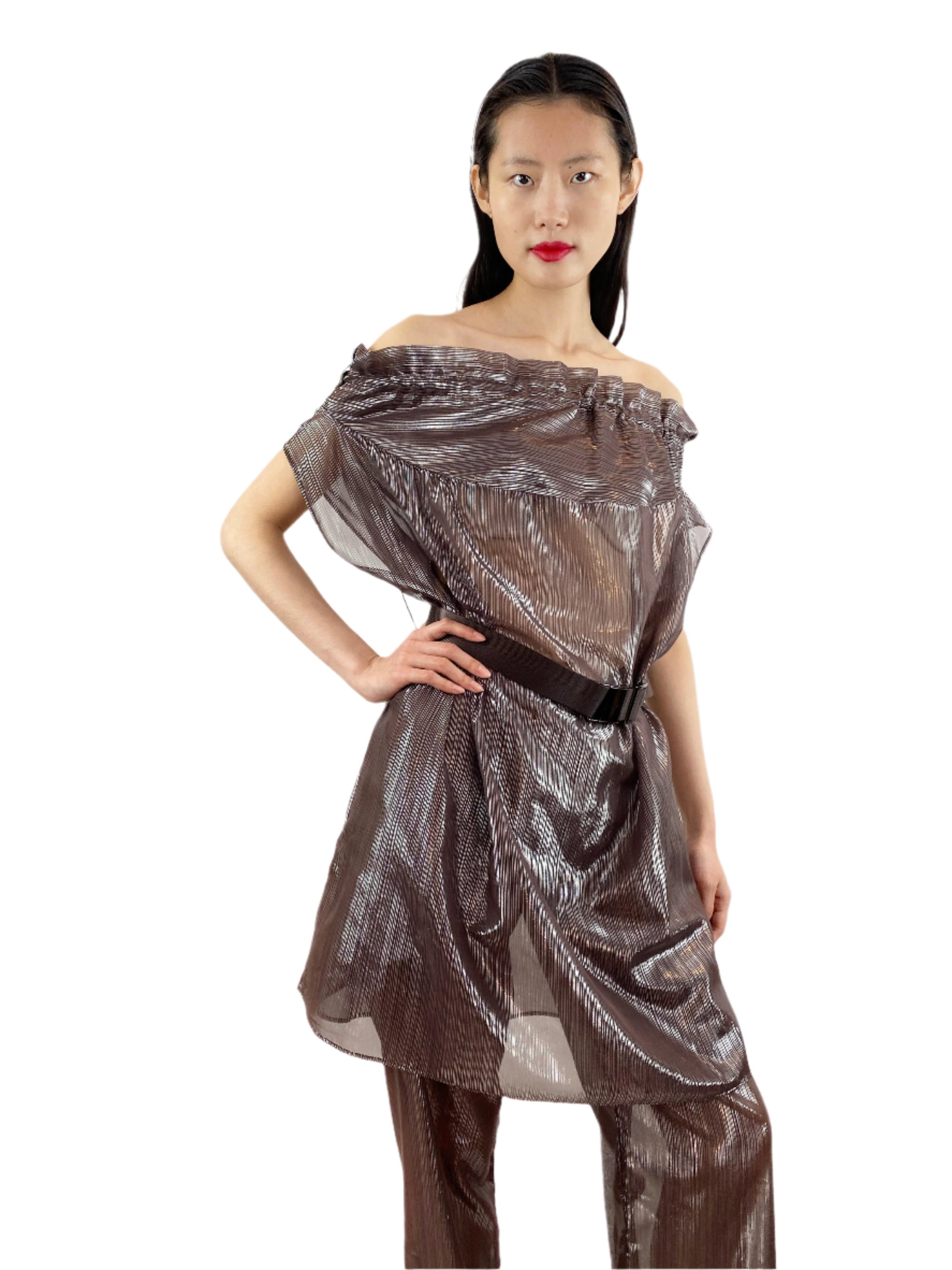 A woman in a sheer bronze overall with a waist-belt stands confidently, exuding modern style and sophistication.