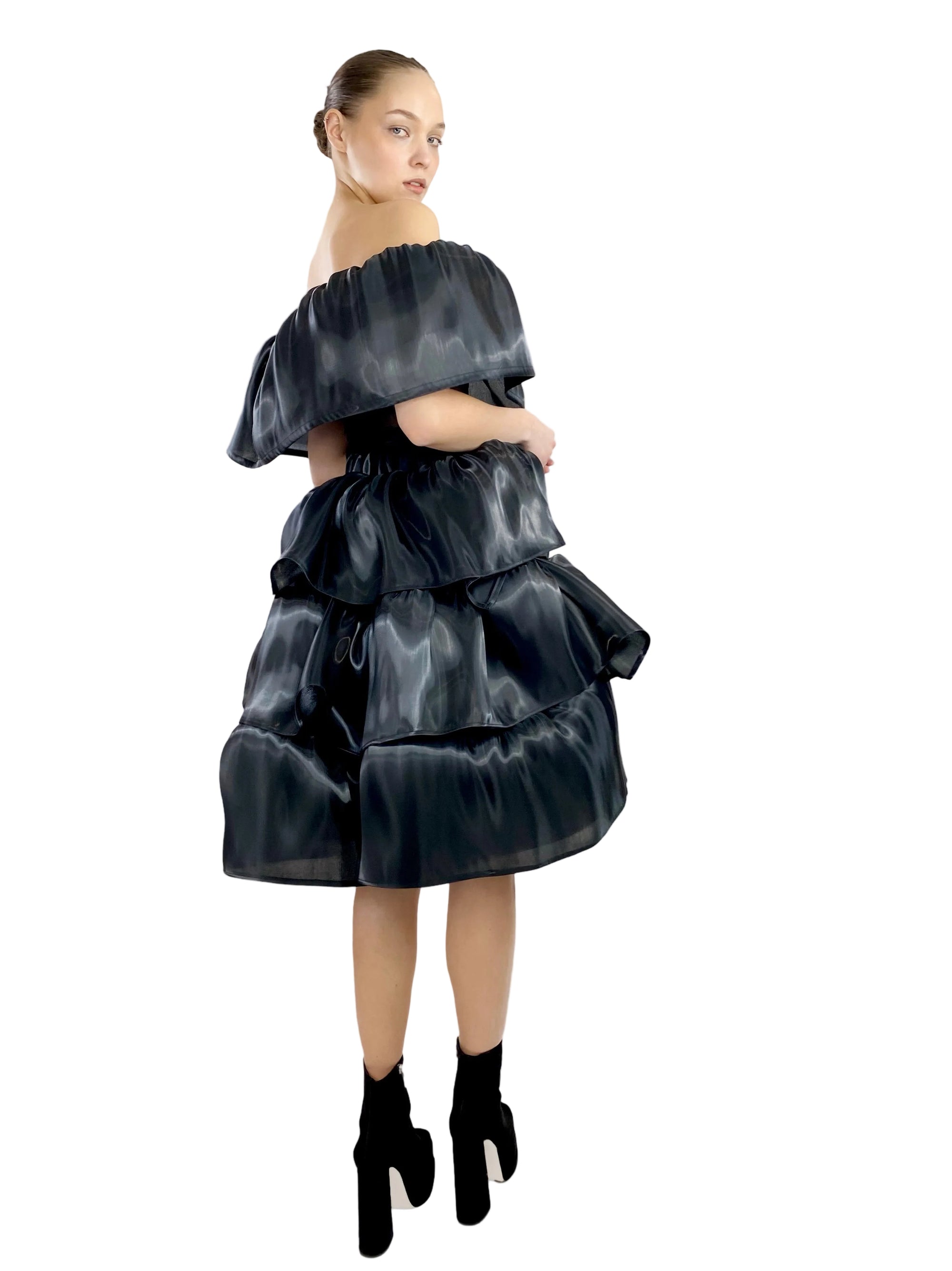 Woman wearing a black off-shoulder dress with layered skirt on a white background