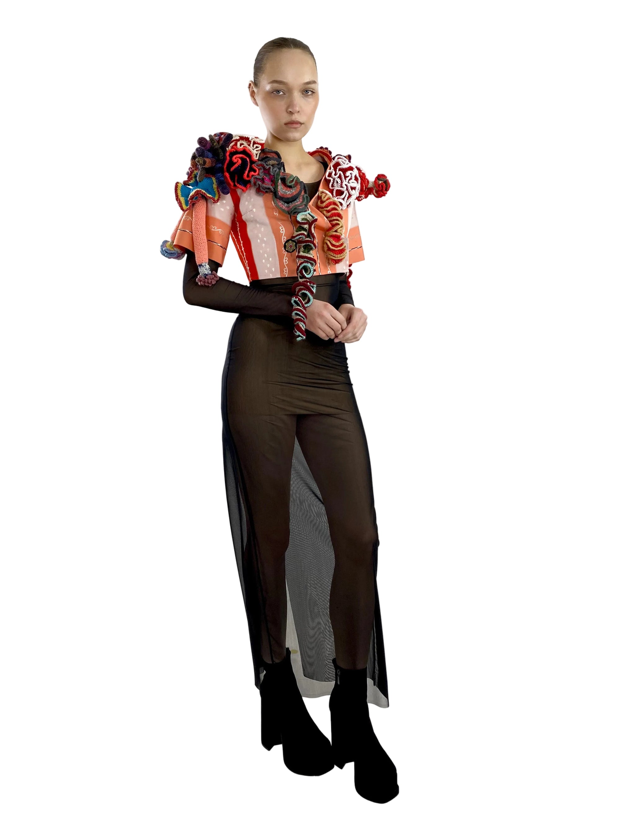 Model wearing a colorful, intricate top with sheer black pants on a white background