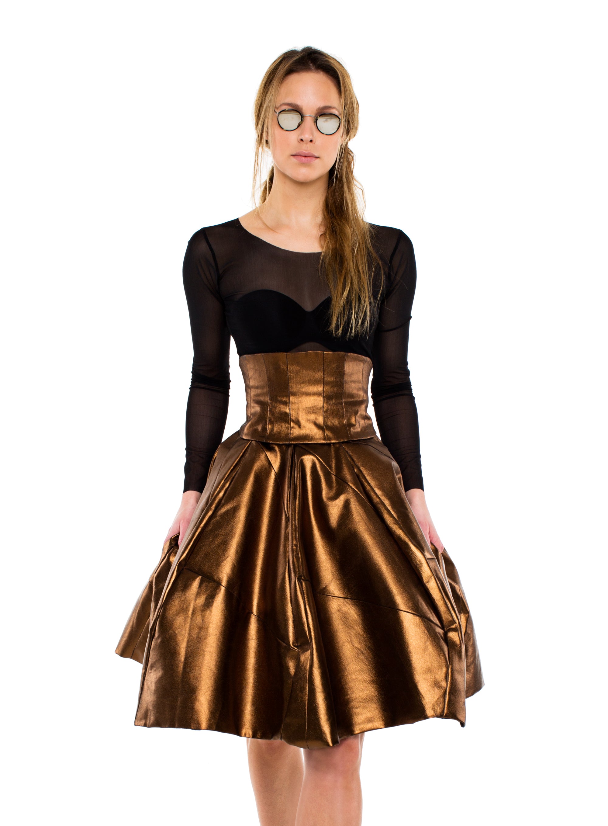 A woman wearing a bronze metallic skirt and a black top stands confidently, showcasing her stylish outfit.