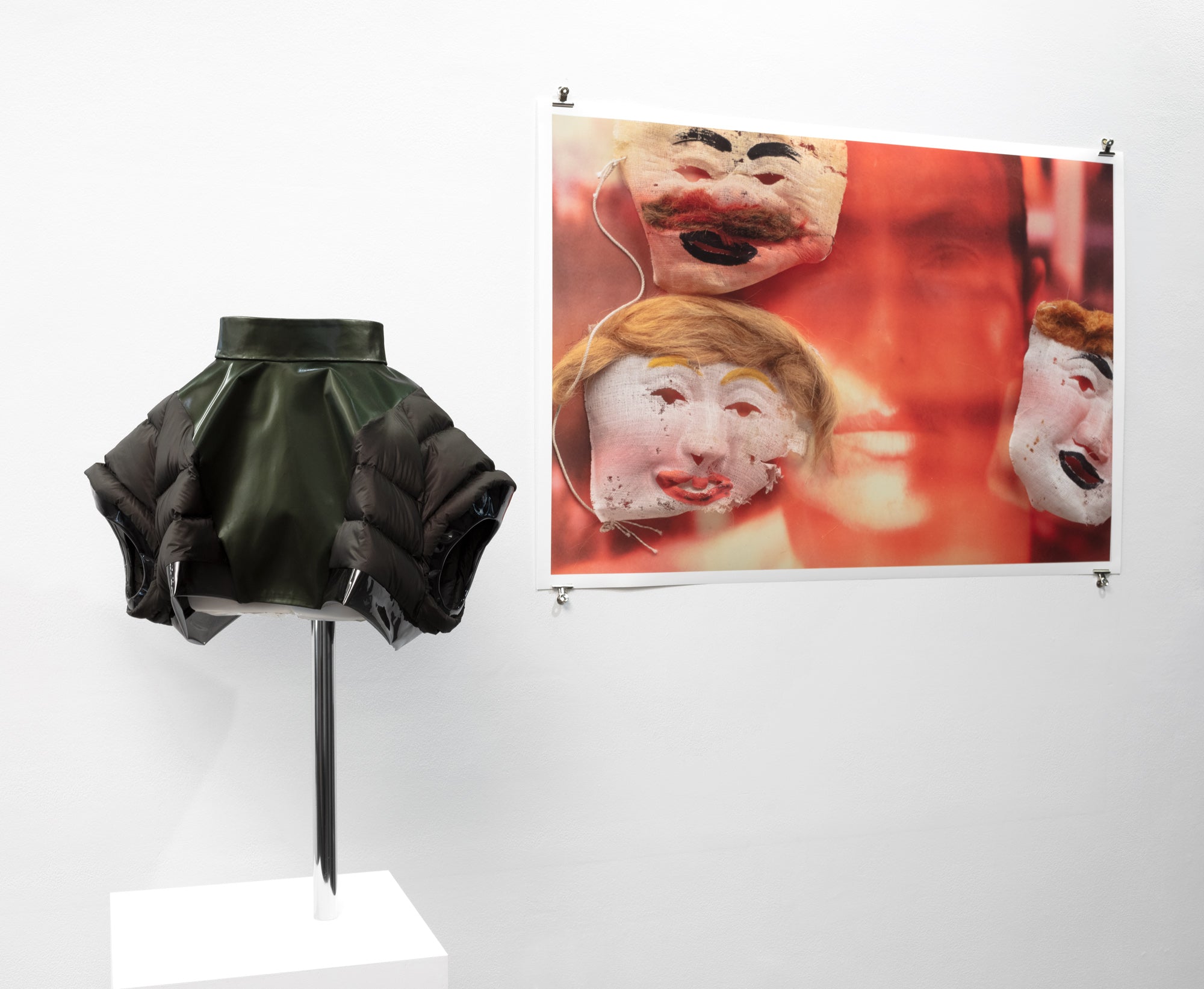 A skirt displayed on a white pedestal, accompanied by a photo of face masks, highlighting themes of identity and protection.