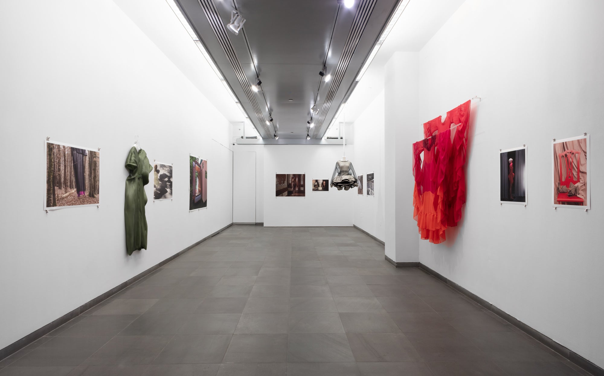 An art gallery featuring multiple photographs and dresses displayed on the walls, showcasing various artistic styles and colors.